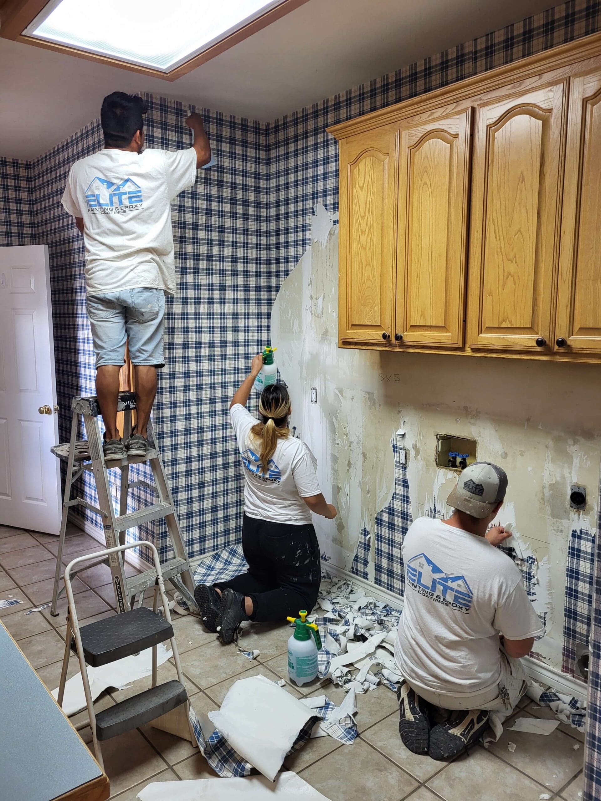 Three men in work clothes painting a kitchen with brushes and rollers.