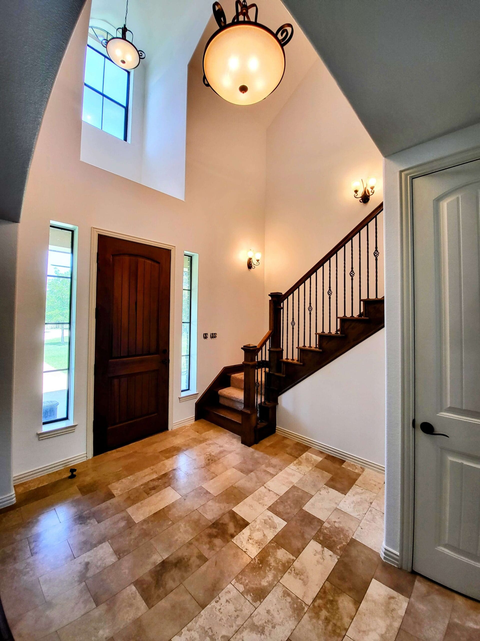 A spacious foyer with a wooden staircase and polished floors, and white painted walls